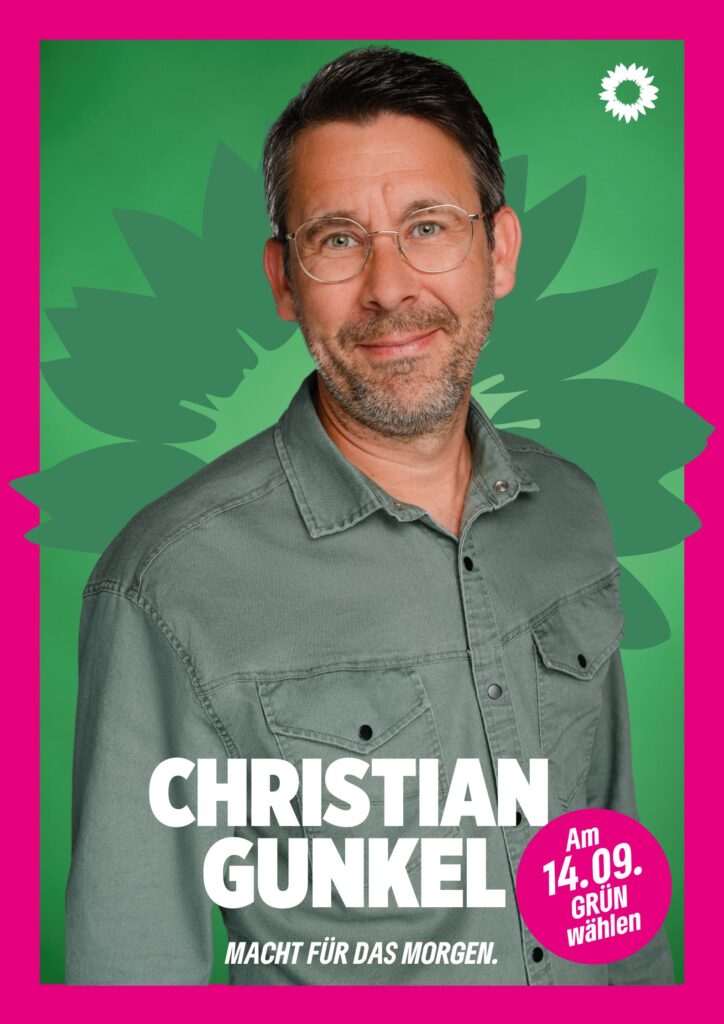 Portraitaufnahme von Christian Gunkel als Wahlplakat mit grüner Sonnenblume im Hintergrund, weißer kleiner Sonnenblume oben rechts, seinem Namen, einem Button mit dem Text "Am 14.09. Grün wählen" und dem Claim Macht für das Morgen.