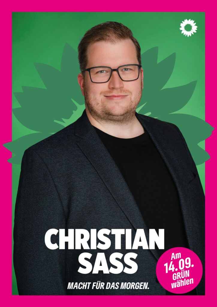 Portraitaufnahme von Christian Sass als Wahlplakat mit grüner Sonnenblume im Hintergrund, weißer kleiner Sonnenblume oben rechts, seinem Namen, einem Button mit dem Text "Am 14.09. Grün wählen" und dem Claim Macht für das Morgen.