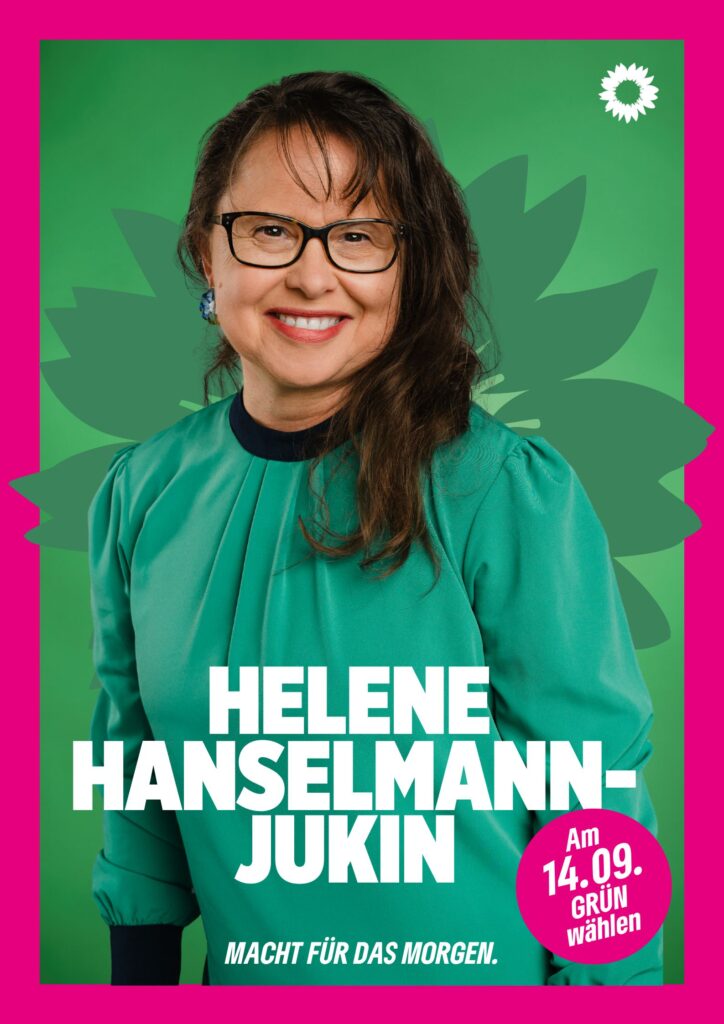 Portraitaufnahme von Helene Hanselmann-Jukin als Wahlplakat mit grüner Sonnenblume im Hintergrund, weißer kleiner Sonnenblume oben rechts, seinem Namen, einem Button mit dem Text "Am 14.09. Grün wählen" und dem Claim Macht für das Morgen.