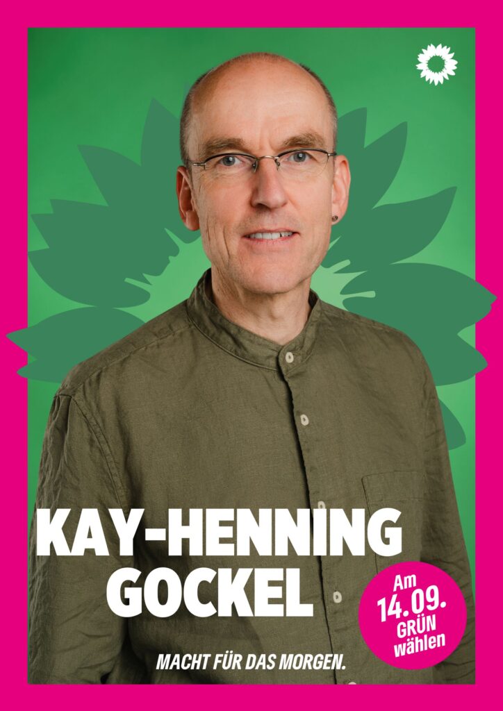 Portraitaufnahme von Kay-Henning Gockel als Wahlplakat mit grüner Sonnenblume im Hintergrund, weißer kleiner Sonnenblume oben rechts, seinem Namen, einem Button mit dem Text "Am 14.09. Grün wählen" und dem Claim Macht für das Morgen.