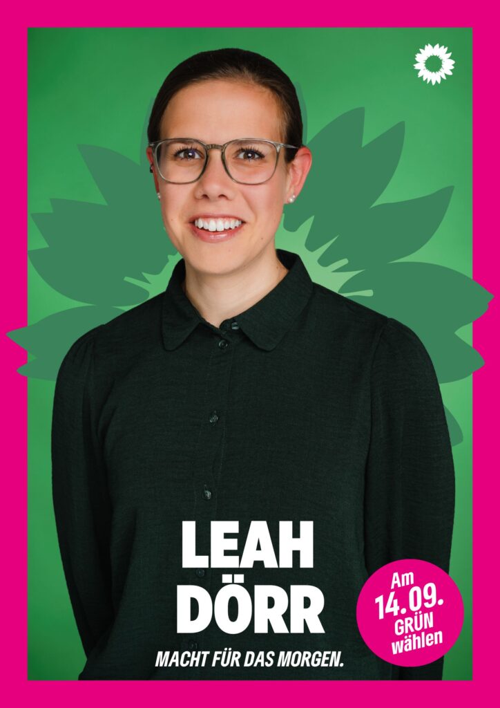 Portraitaufnahme von Leah Dörr als Wahlplakat mit grüner Sonnenblume im Hintergrund, weißer kleiner Sonnenblume oben rechts, seinem Namen, einem Button mit dem Text "Am 14.09. Grün wählen" und dem Claim Macht für das Morgen.