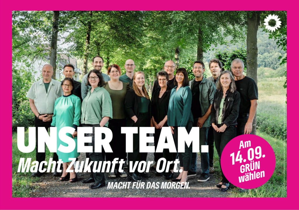 Wahlplakat mit pinkem Rand mit 15 Personen auf einem Schotterweg mit Gras an beiden Seiten vor einer Allee und dem Slogan Unser Team. Macht Zukunft vor Ort. und dem Claim ganz unten Macht für das Morgen. Unten rechts einen pinken Kreis mit dem Slogan "Am 14.09. GRÜN wählen"